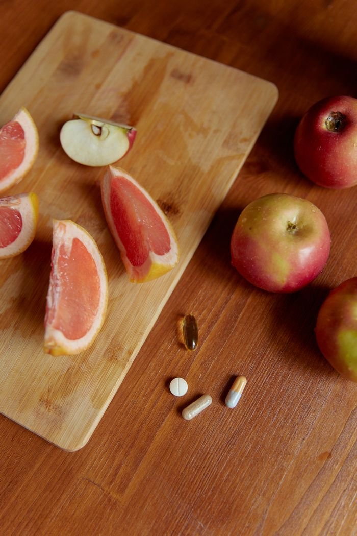 A close-up of apples, grapefruit slices, and vitamins on a wooden board promoting healthy eating.